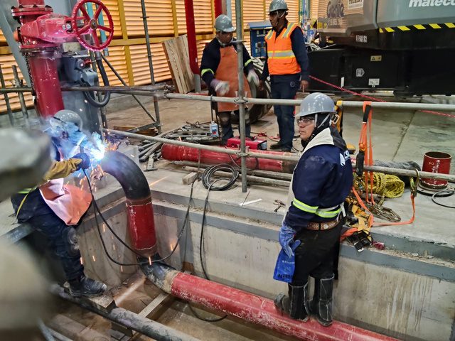 Soldadores trabajando sobre tubería roja de red contra incendio dentro de planta industrial