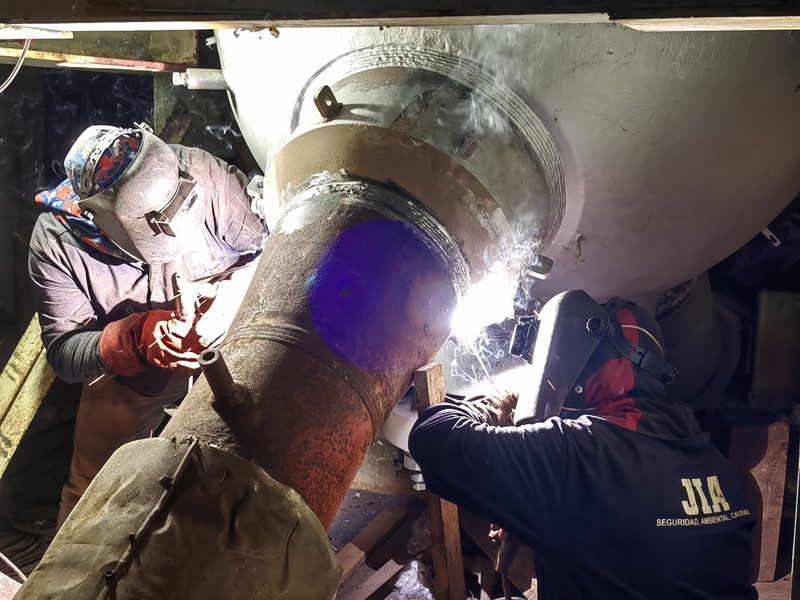 Dos soldadores con careta ejecutando soldadura en tubería de gran diámetro con arco eléctrico