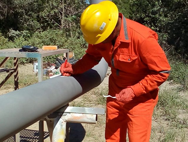 Operador con casco y overol aplicando recubrimiento sobre tubería en campo