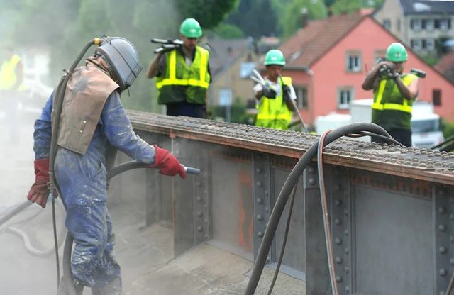 Operador con capucha de sandblast limpiando estructura metálica